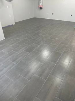 Gray tiled floor in a room under construction. Walls are gray, with some electrical outlets visible.