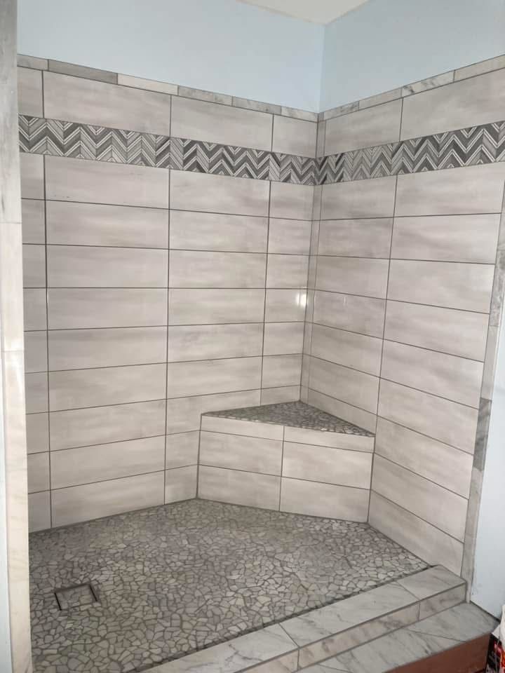 Tiled shower with pebble floor and built-in corner seat. Gray and white tiles with decorative border.