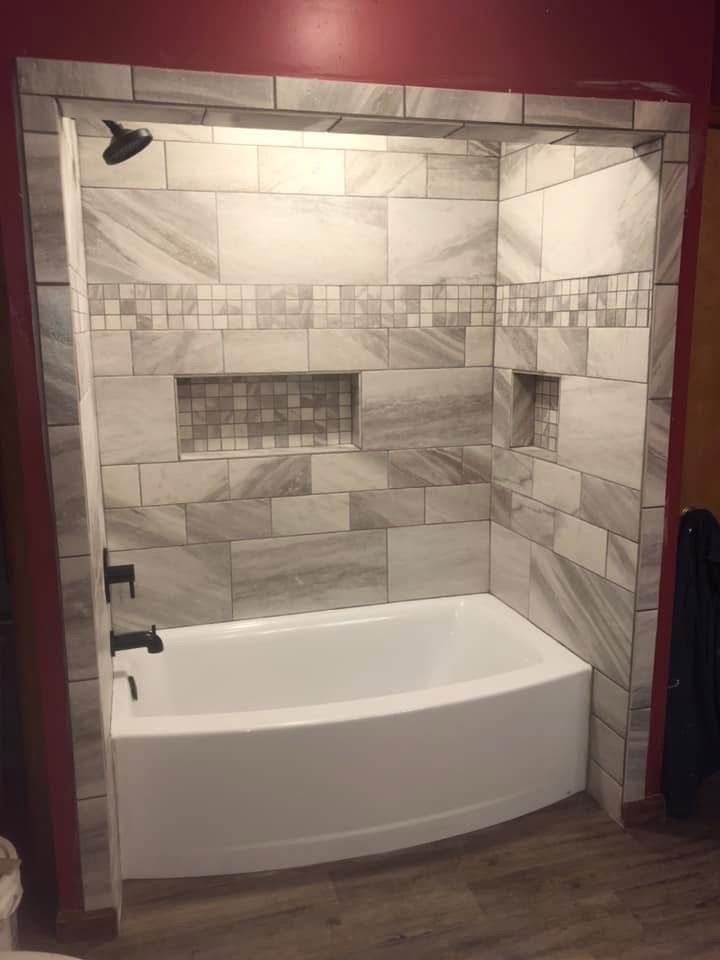 Bathroom with white bathtub, tiled shower with built-in shelves, and dark fixtures.