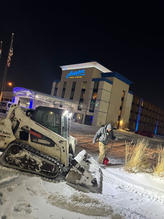 A man is plowing snow in front of a hotel at night.