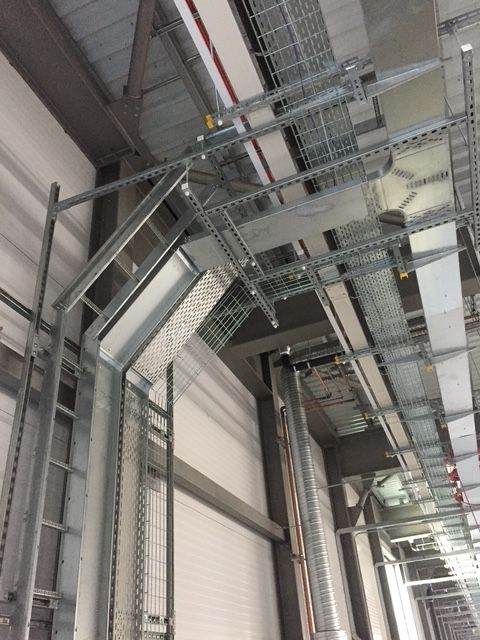 Industrial metal cable trays and support struts mounted to a building's ceiling and wall structure.
