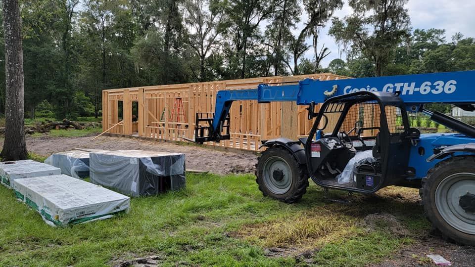 Construction site: wooden structure being built, a blue forklift, and wrapped materials on the ground.