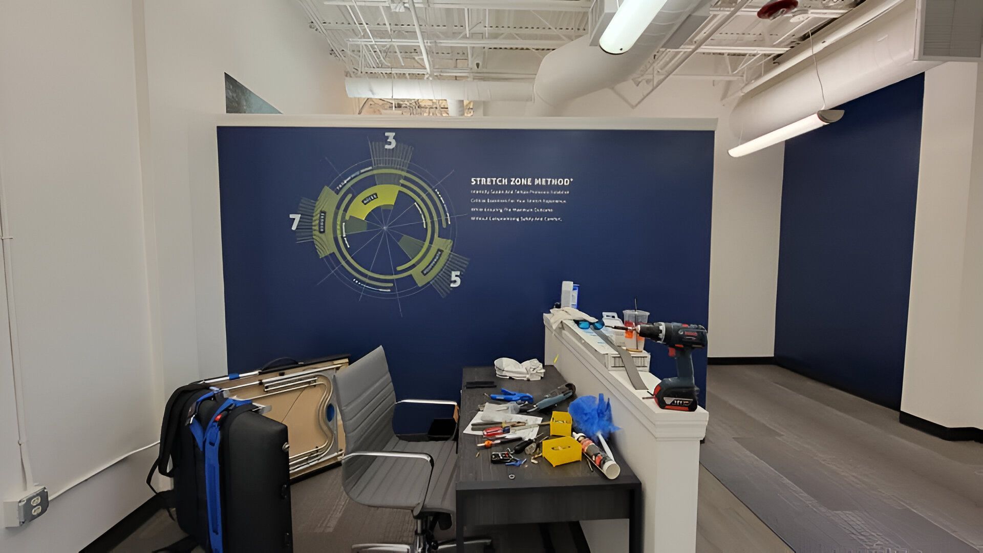 Office space with blue accent wall and desk with items on it. White ceiling with lighting fixtures.