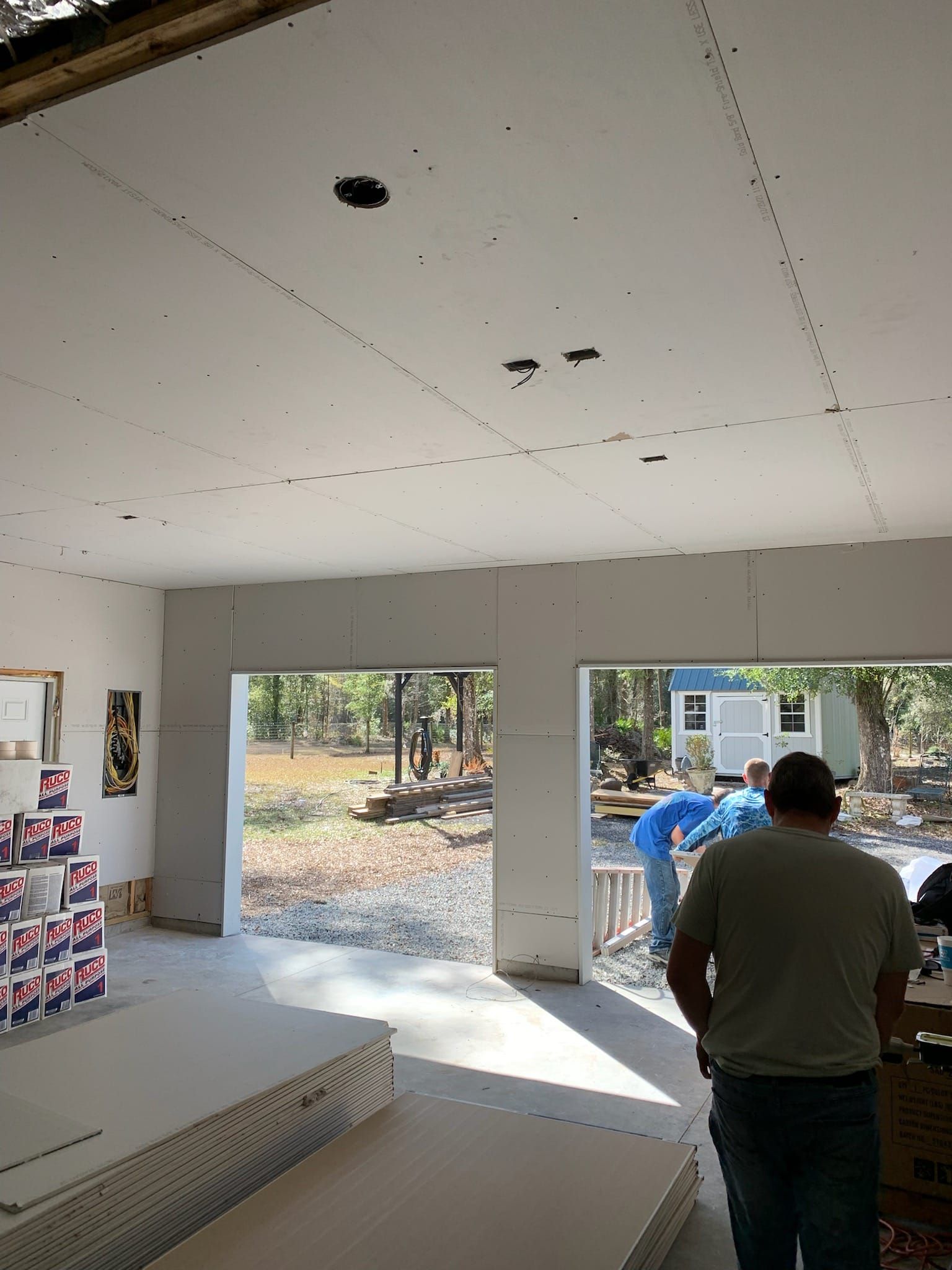 Interior construction scene: Drywall installation, unfinished ceiling, two open doorways, two workers.