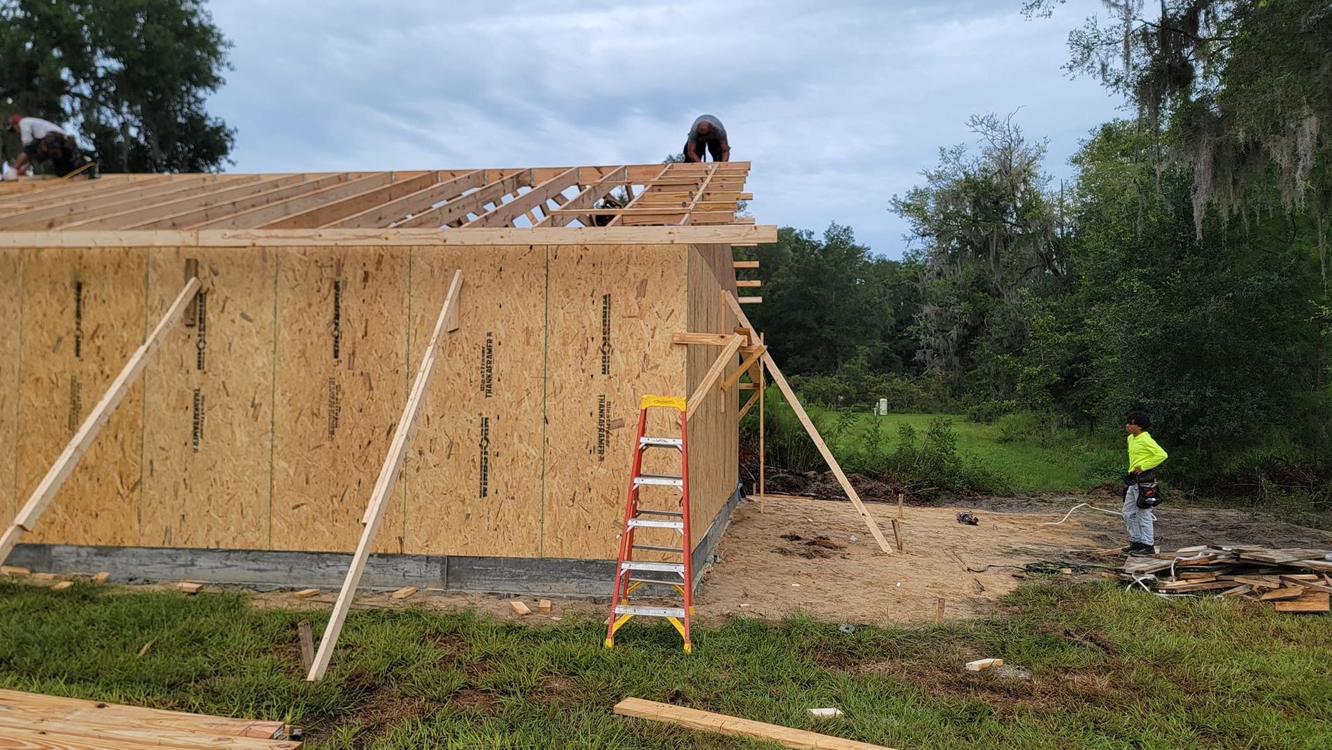 Construction workers building a roof on a wooden structure. A ladder is leaned against the wall.