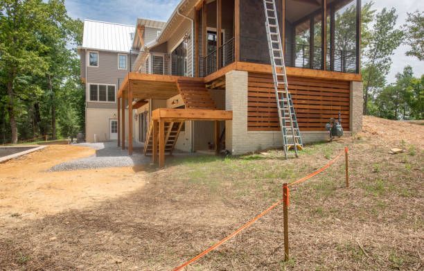 Construction site: Two-story house with unfinished deck, wood siding, ladder, and exposed foundation.