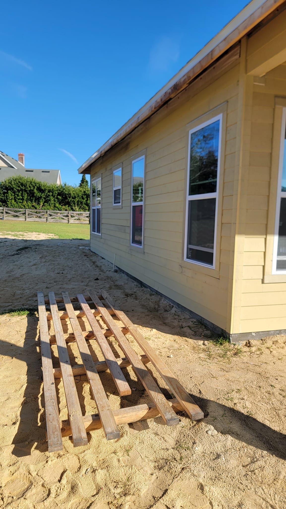 Side view of a yellow house under construction on a sunny day. Wooden planks are on the ground in front.