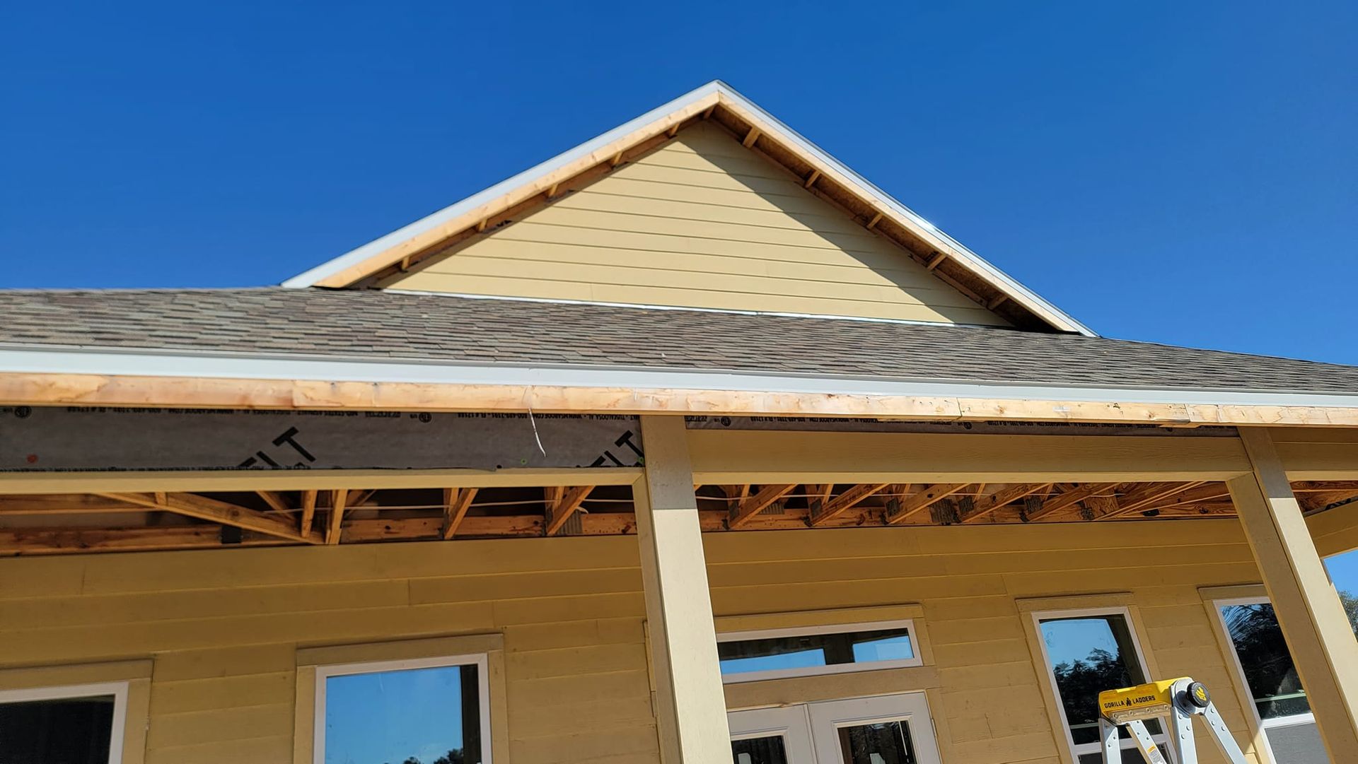 Construction of a house with a light yellow exterior, blue sky, and roof framing.