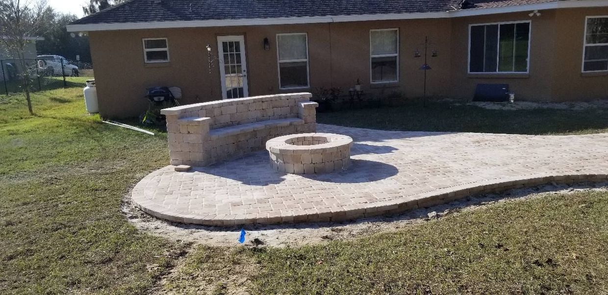Backyard patio with a built-in bench and fire pit, adjacent to a brown brick house.