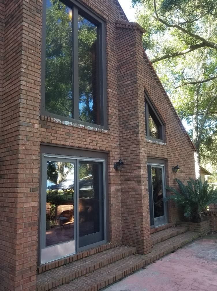 Brick house exterior with large windows, a small porch, and trees in the background.