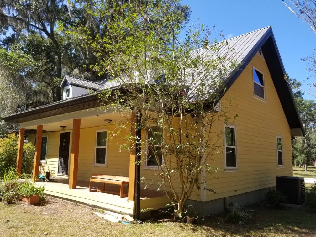 Yellow house with porch and metal roof, small tree in front.