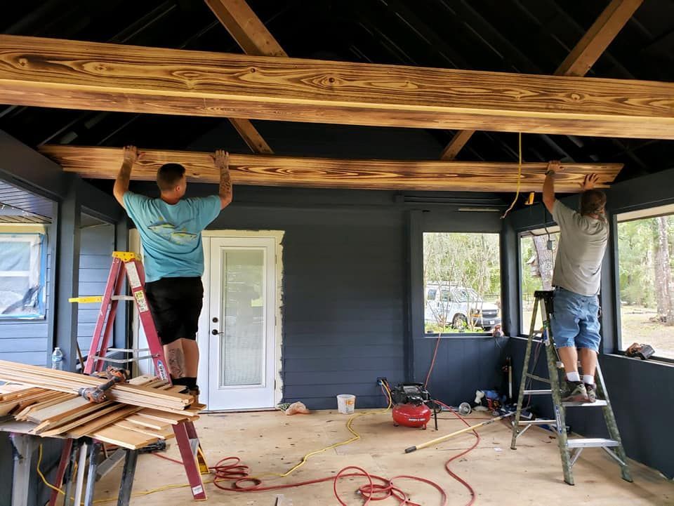 Two men installing wooden beams on a porch ceiling; tools and supplies visible.