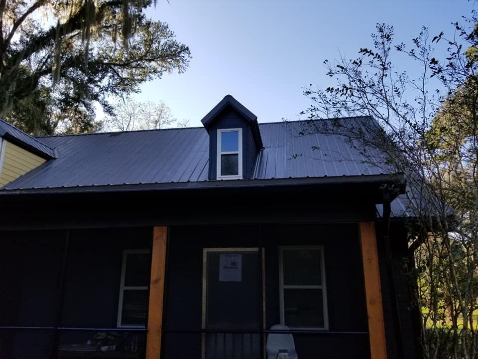 Dark blue house with metal roof, dormer window, and wooden porch supports.