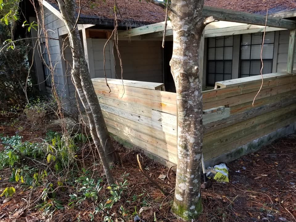 A dilapidated building with exposed wood siding. Trees obscure parts of the structure.