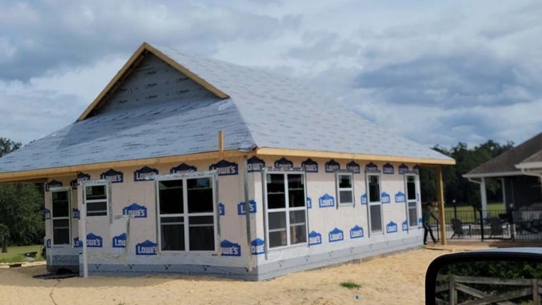 House under construction with blue paper and windows, unfinished roof, in daylight.