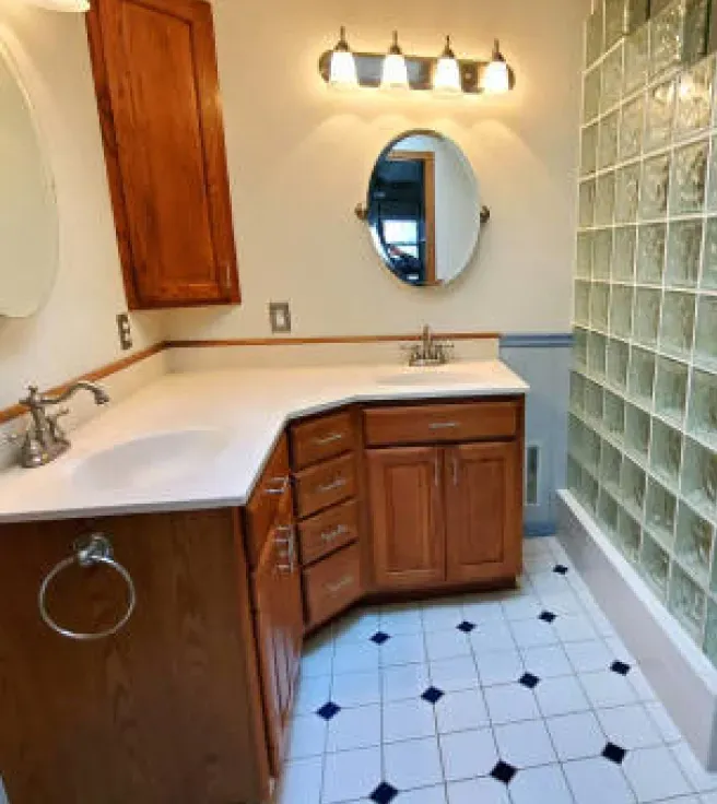 Bathroom with a vanity, mirror, and glass block shower. The floor is tiled with blue and black accents.