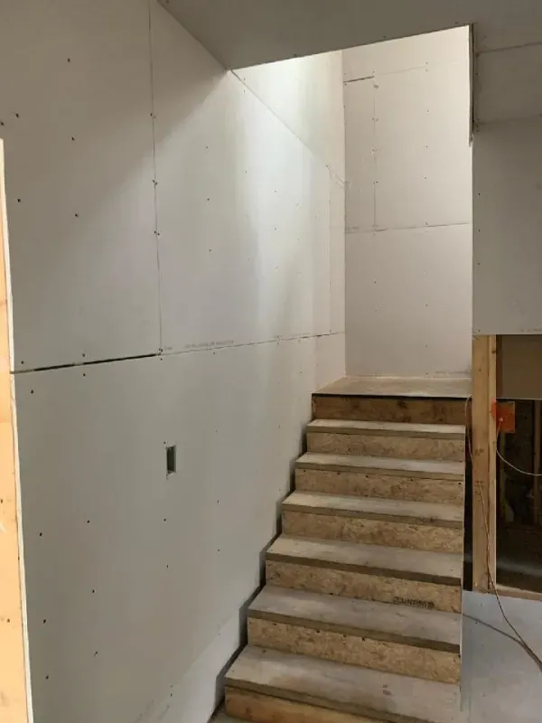 Staircase ascending into a doorway in a room with drywall. Unfinished wooden steps, white walls.