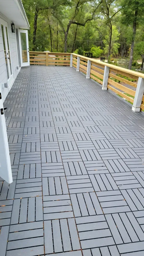 Gray tile deck with wooden railings and a white house.