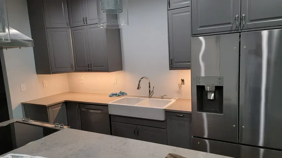 Gray kitchen with stainless steel refrigerator, white farmhouse sink, and gray cabinets.