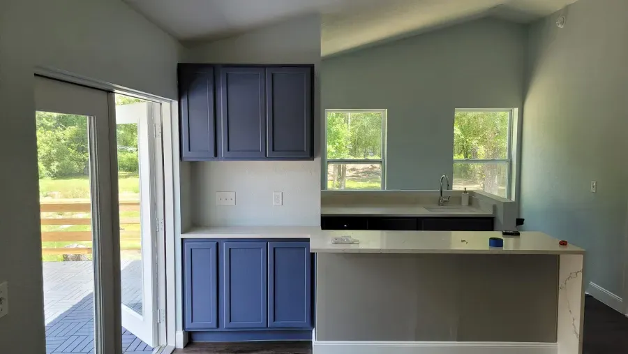 Interior view of kitchen with blue cabinets, white countertop, and open door to a patio.