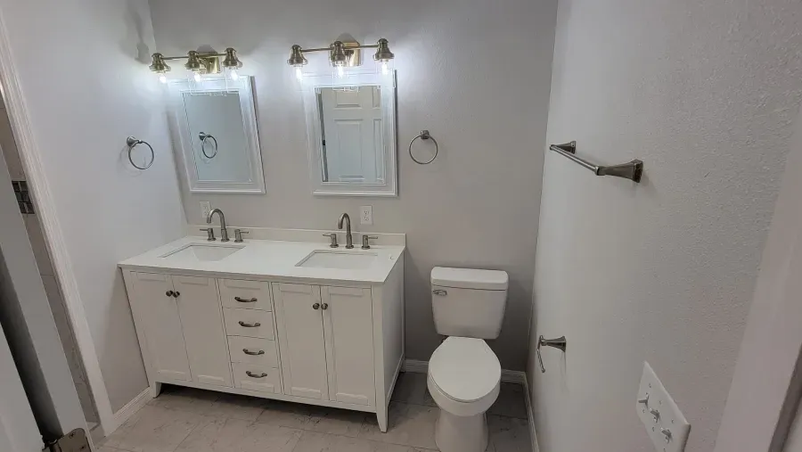 Bathroom with white vanity, two mirrors, and toilet. Light gray walls and floor.
