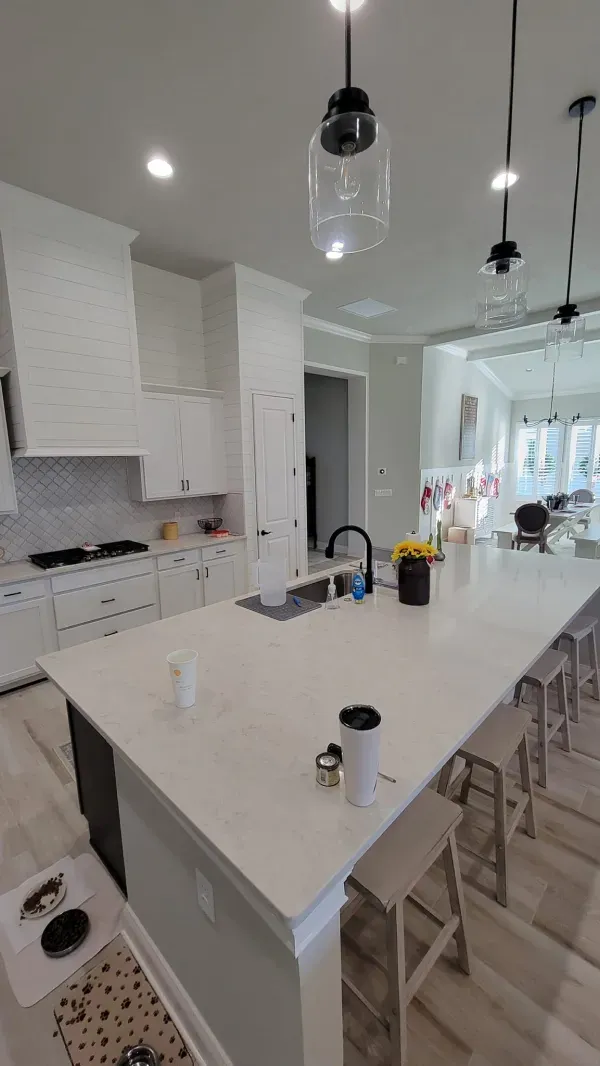 Modern kitchen with white countertops, island, and cabinets; pendant lights hang above.