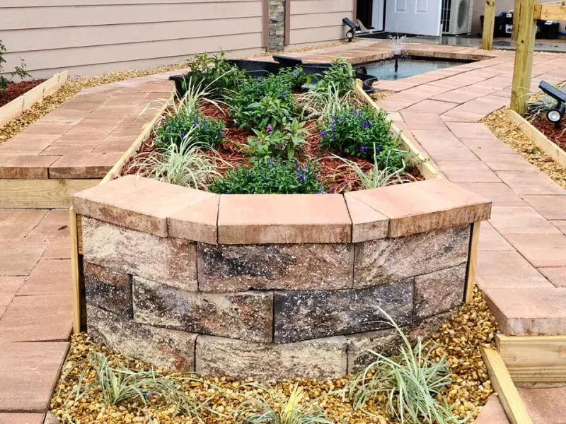 Brick planter with colorful plants surrounded by a brick pathway and tan gravel.