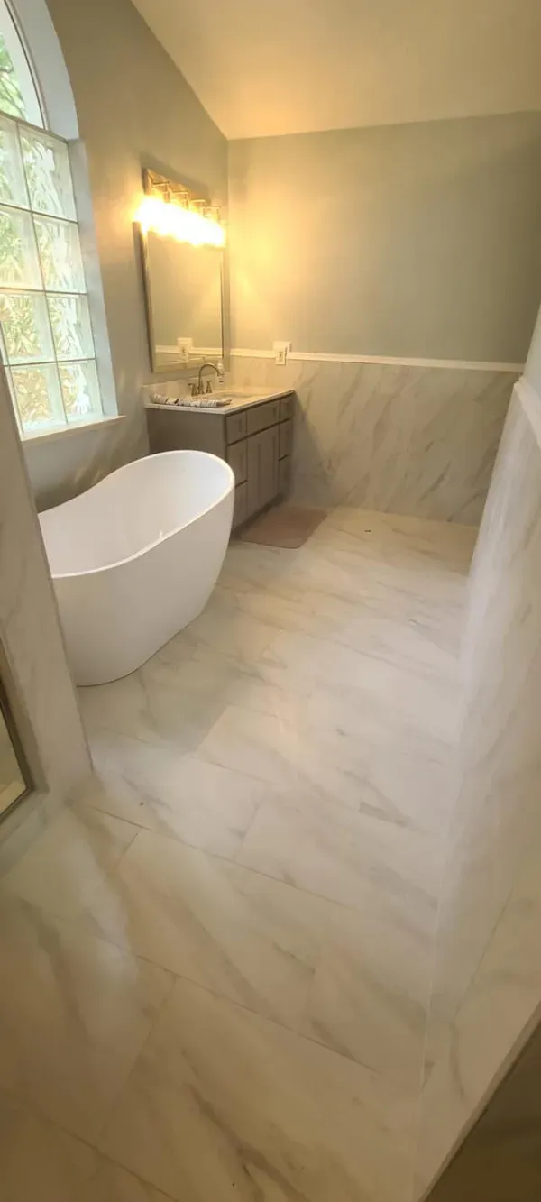 A spacious modern bathroom with a free-standing tub, large window, and marble flooring.
