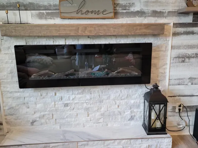 Fireplace with black frame, wooden mantel, and decorative lantern. White stone wall backdrop.