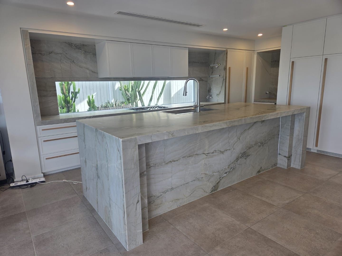 Modern kitchen with large marble island, white cabinets, and large window — Southeast Stone Pty Ltd In Caloundra West, QLD