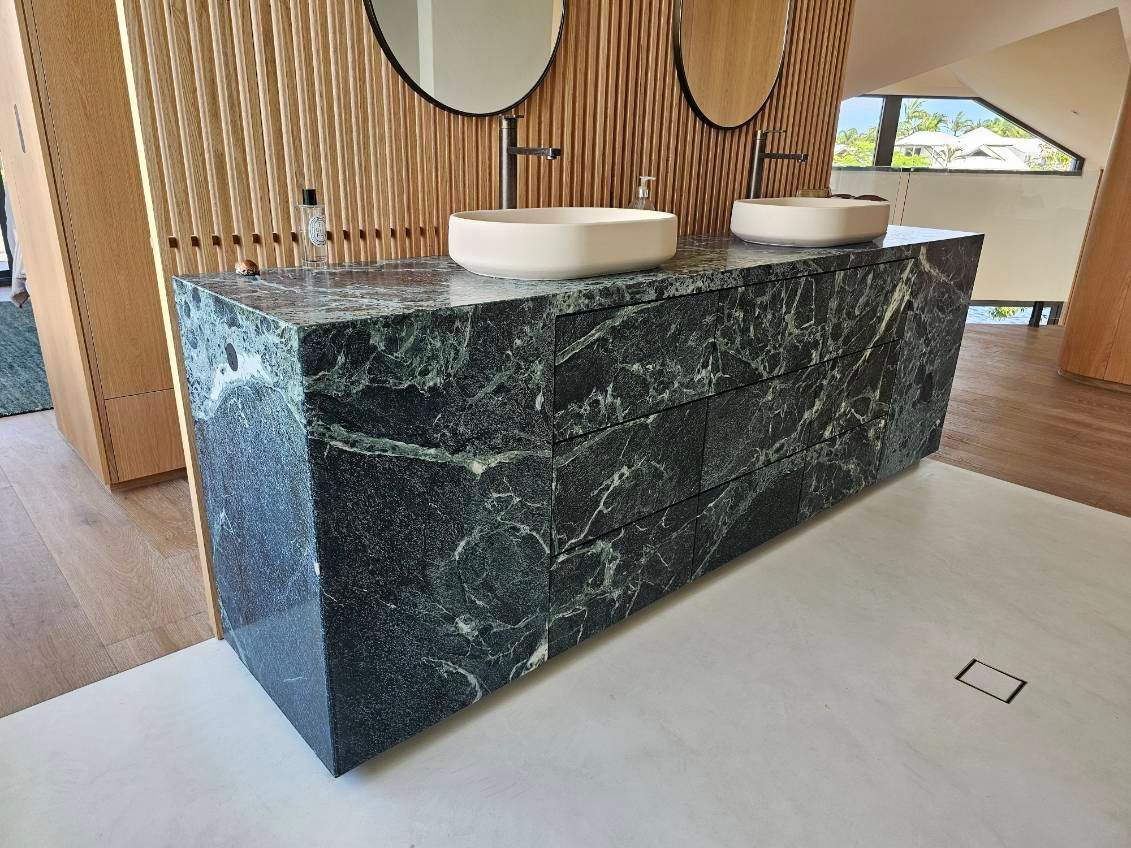 Dark green marble vanity with two sinks, two round mirrors, and wooden slatted wall in a bathroom — Southeast Stone Pty Ltd In Caloundra West, QLD