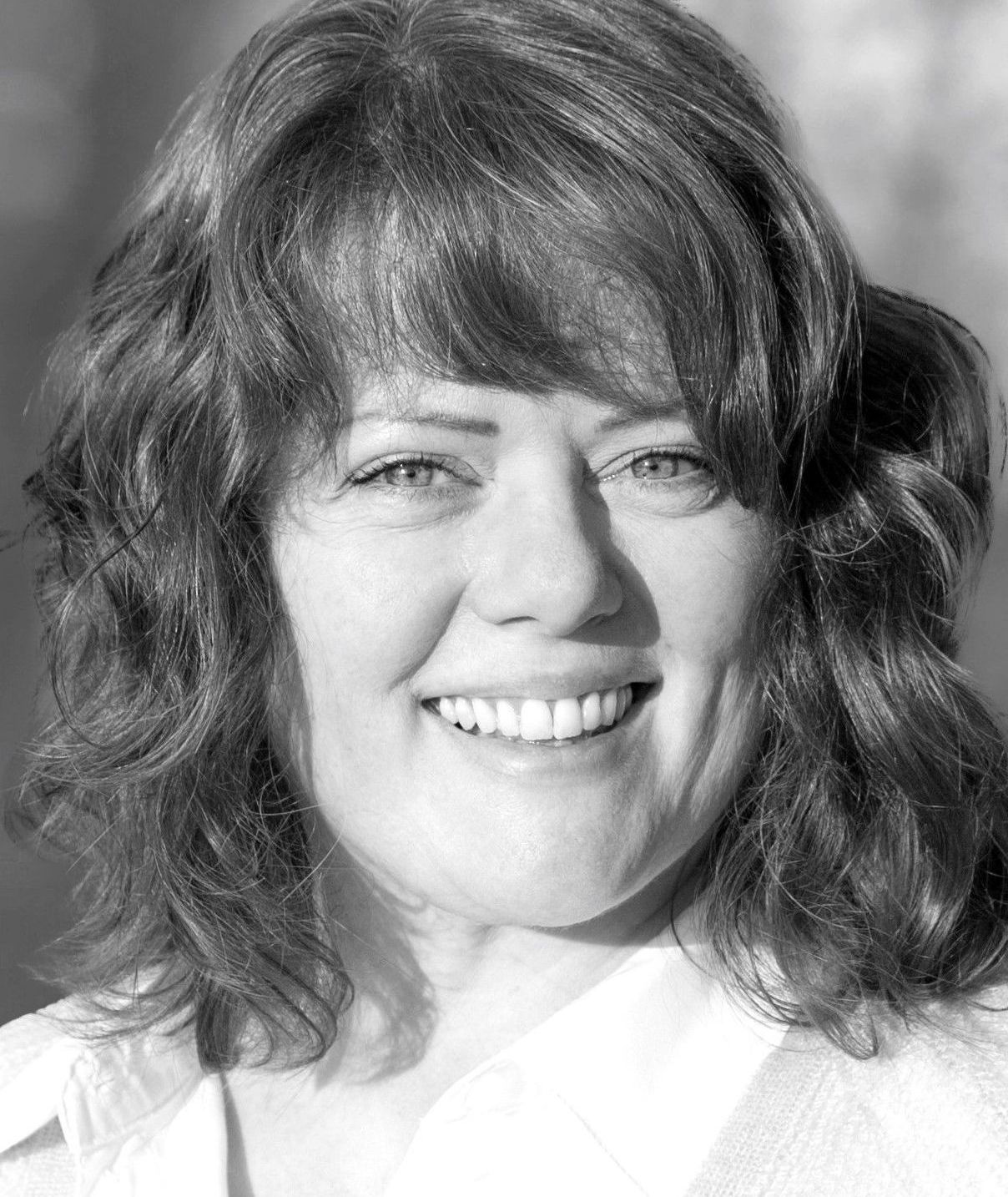 A woman with red hair is smiling in a black and white photo.