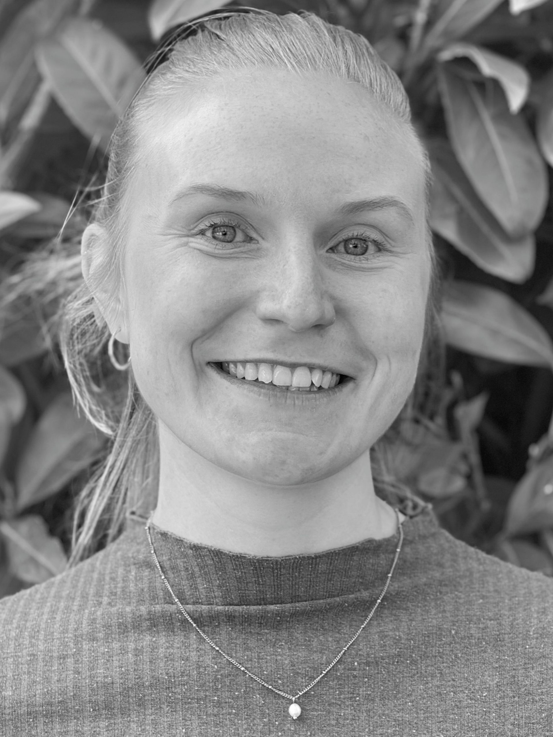 A woman in a black shirt is smiling in a black and white photo.