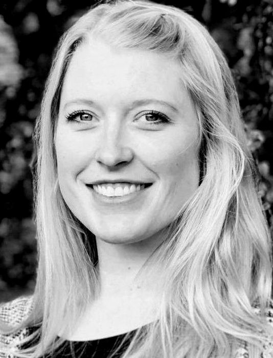 A woman with long blonde hair is smiling in a black and white photo.
