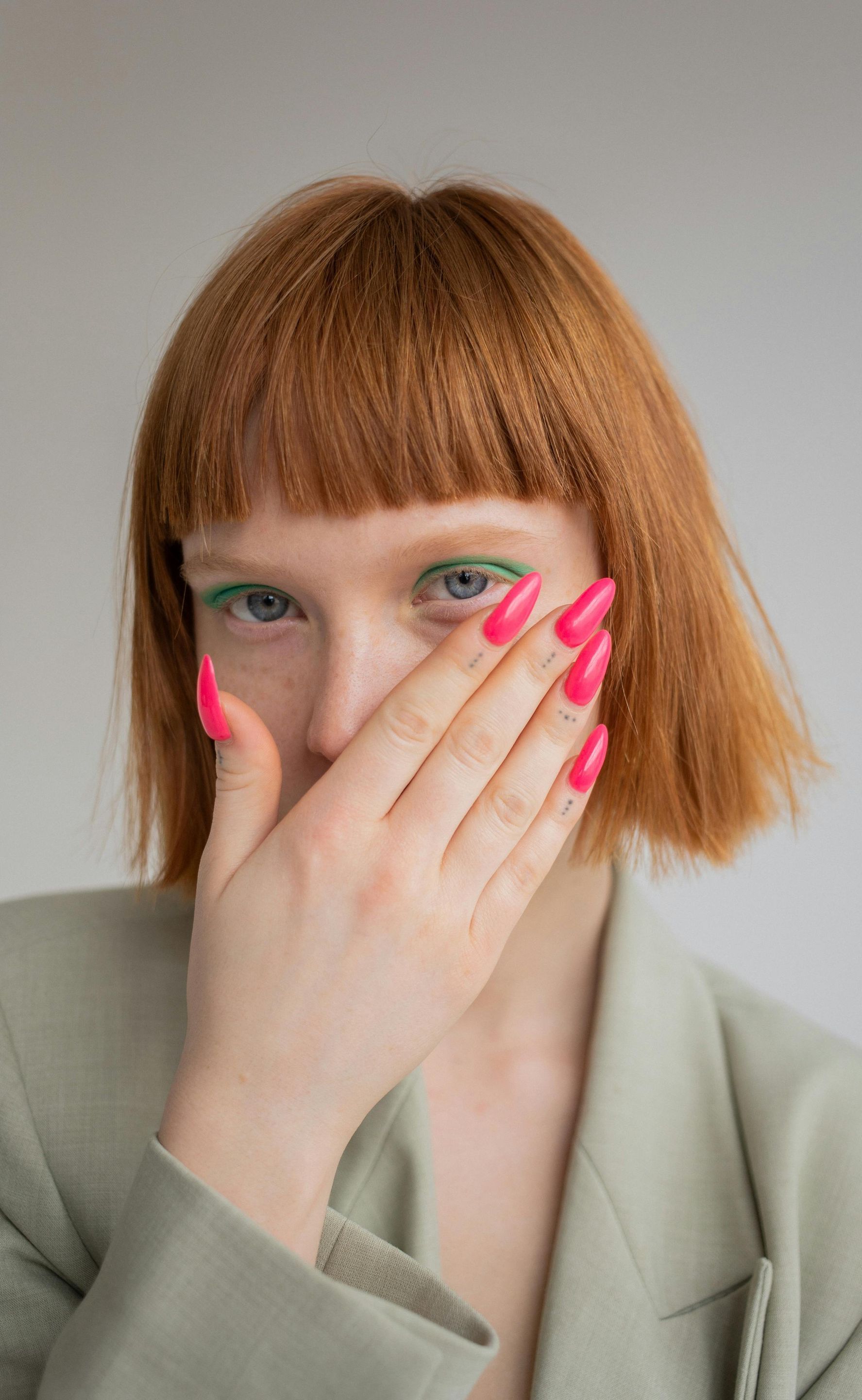 woman with red hair covering her mouth with hand and has a pink manicure .