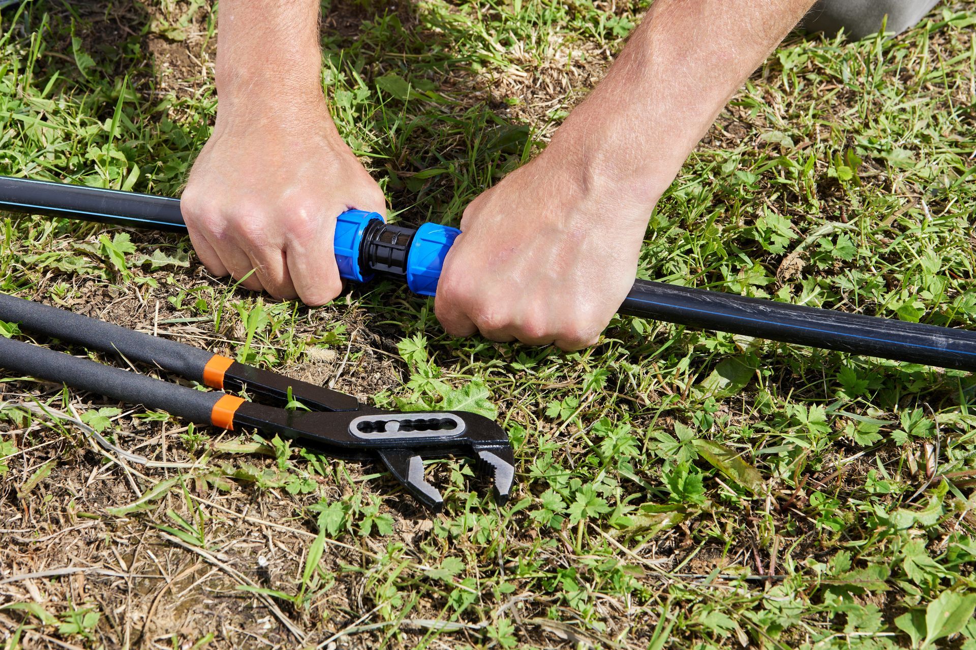 A person is working on a hose with a pair of pliers.