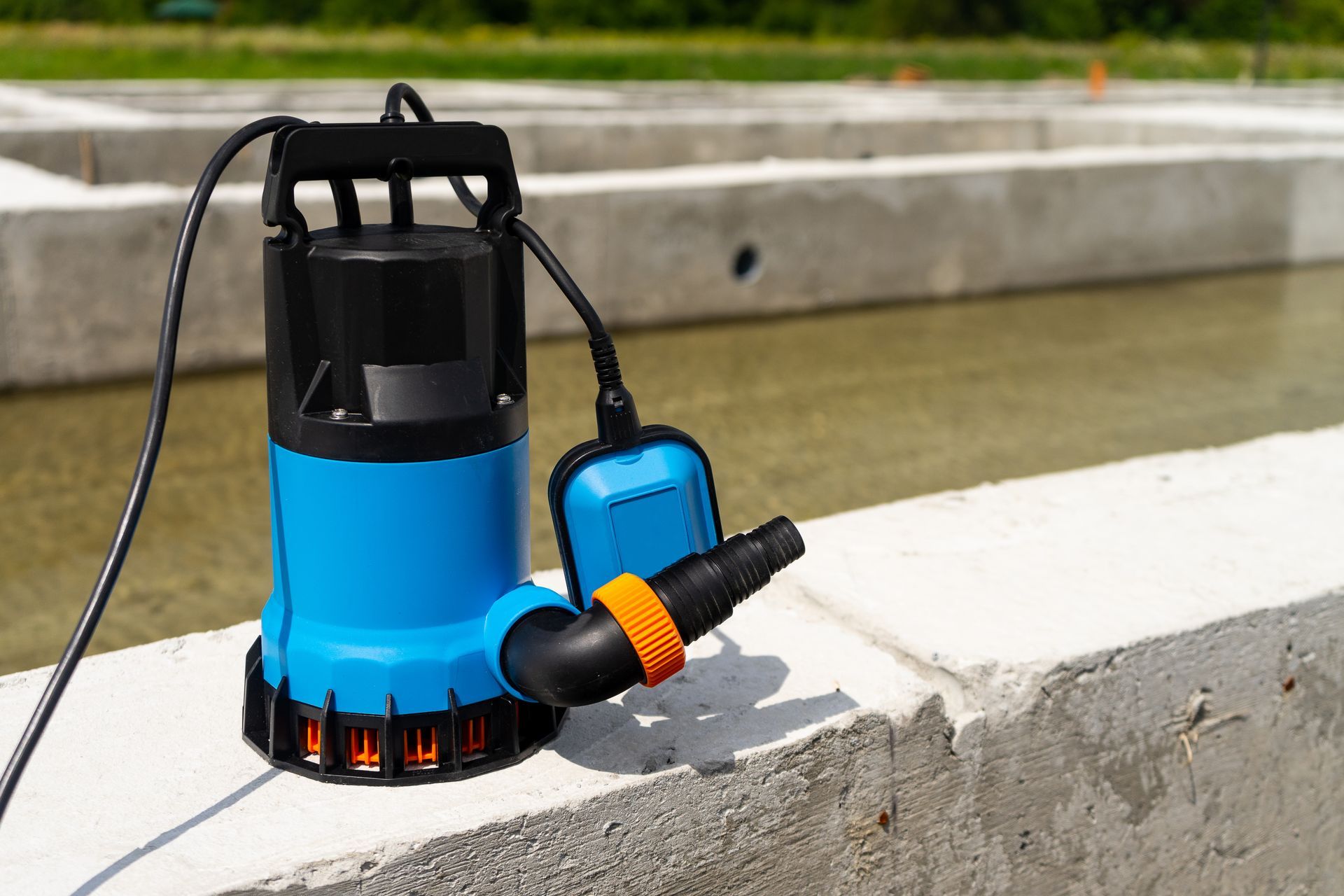 A blue water pump is sitting on a concrete wall next to a pond.