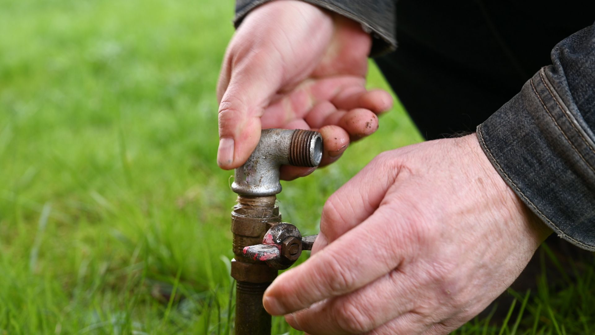 A man is fixing a faucet in the grass.