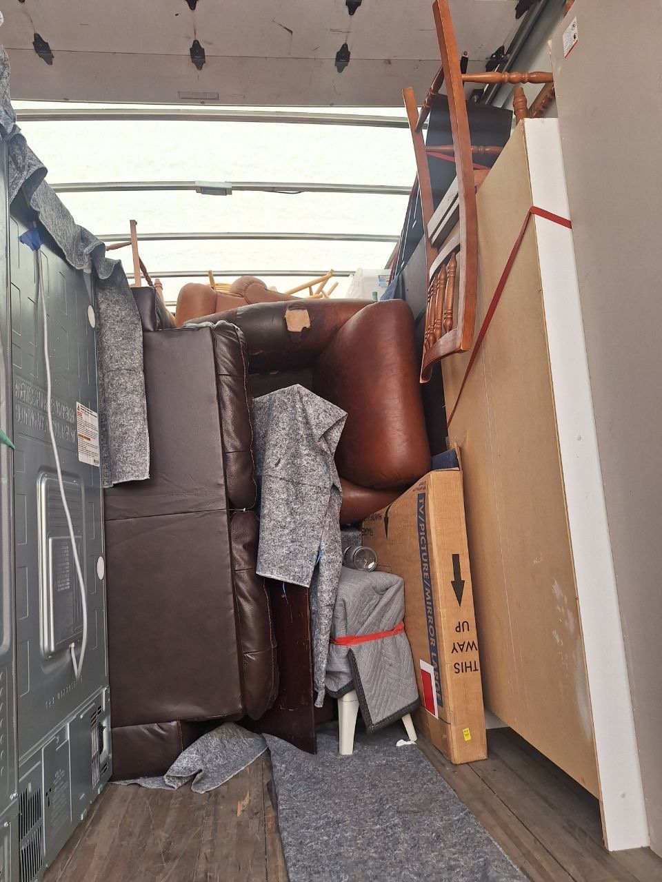 Packed truck interior with stacked brown and gray furniture and boxes filling the cargo area