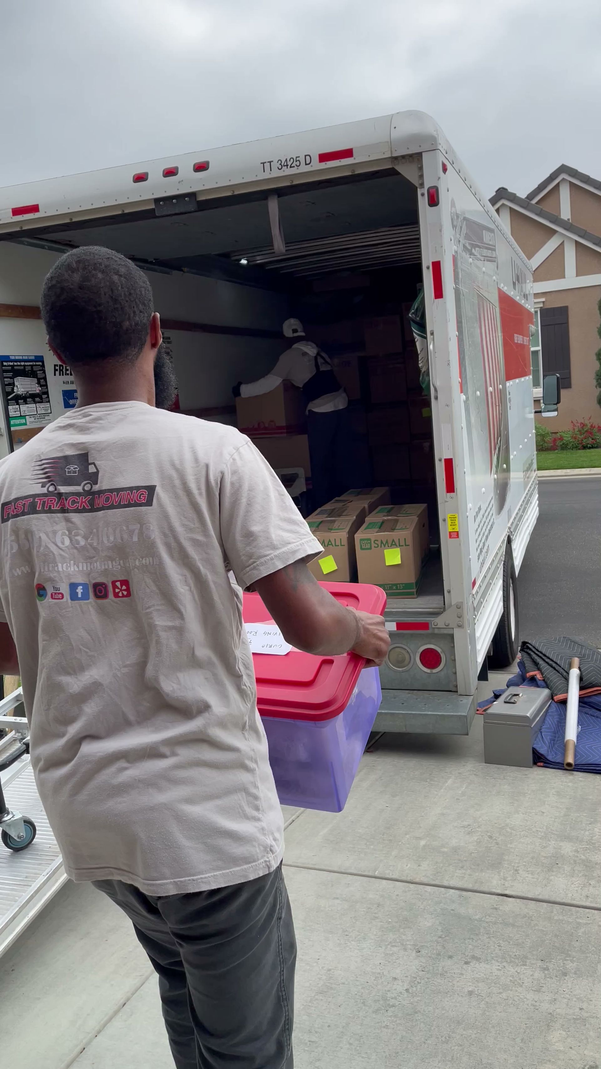 Mover loading boxes into the back of a white moving truck in a suburban driveway.