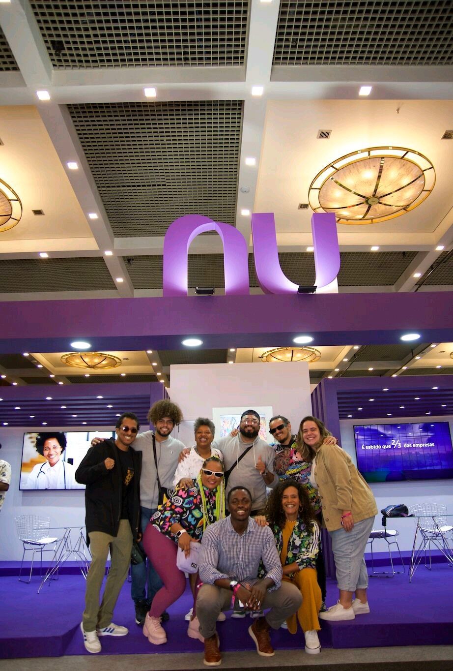 Grupo de pessoas posando em frente a uma placa roxa com a inscrição
