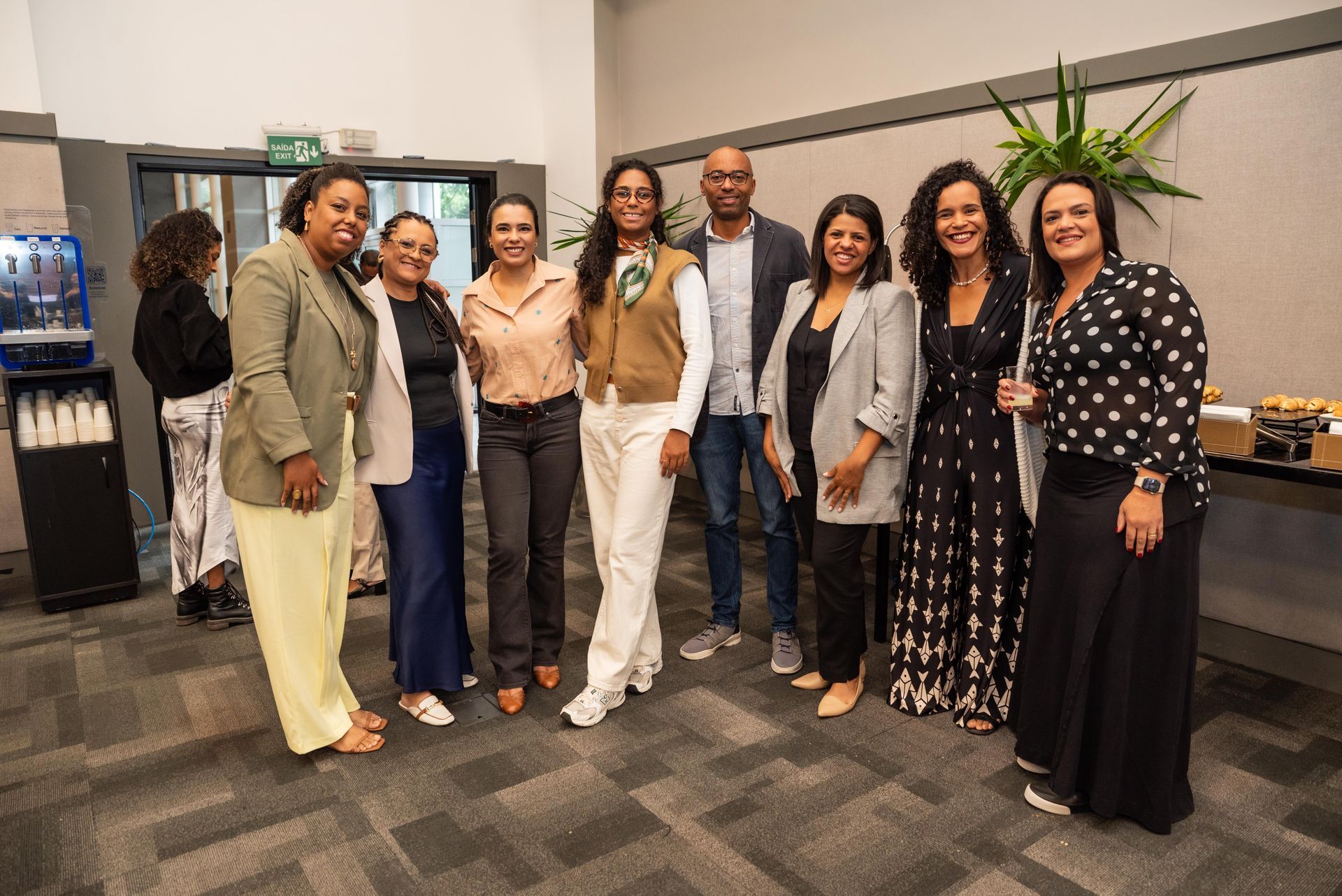 Grupo de pessoas diversas sorrindo para uma foto em um edifício moderno.
