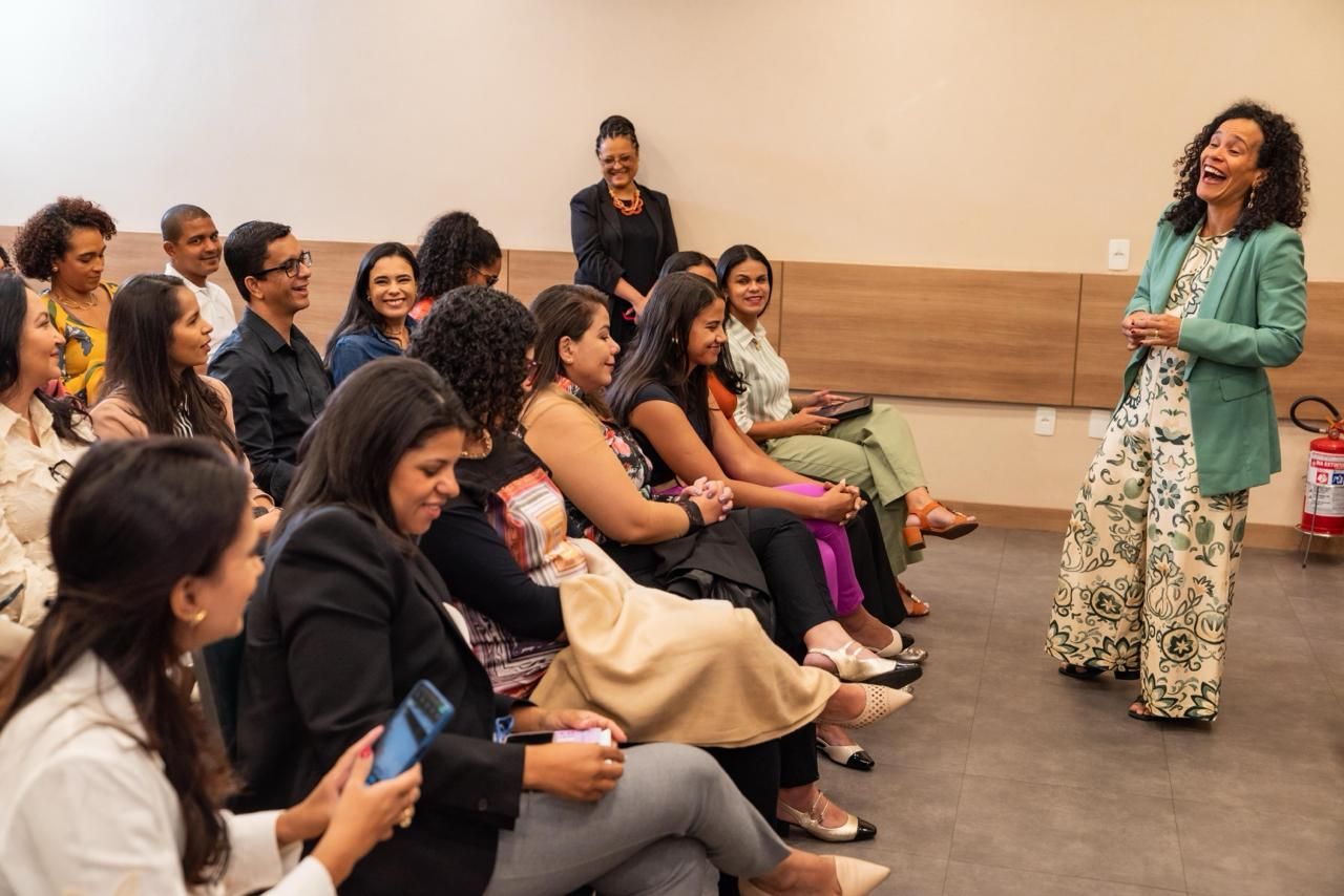 Mulher fazendo uma apresentação para um público diversificado em uma sala. As pessoas sorriem e ouvem.