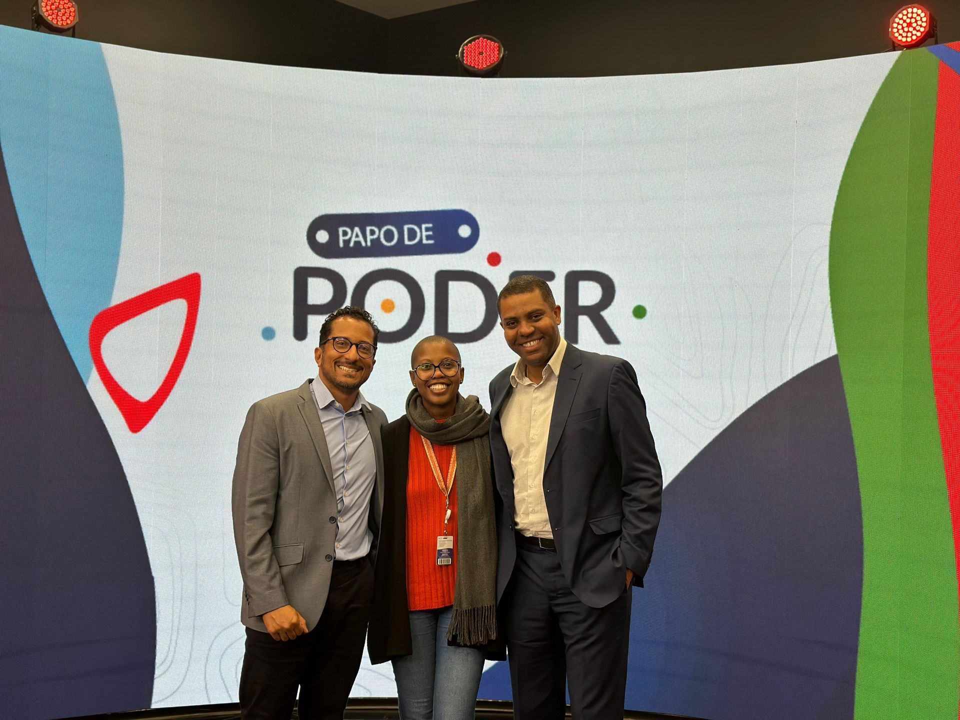 Três pessoas sorrindo em frente a um fundo com a inscrição