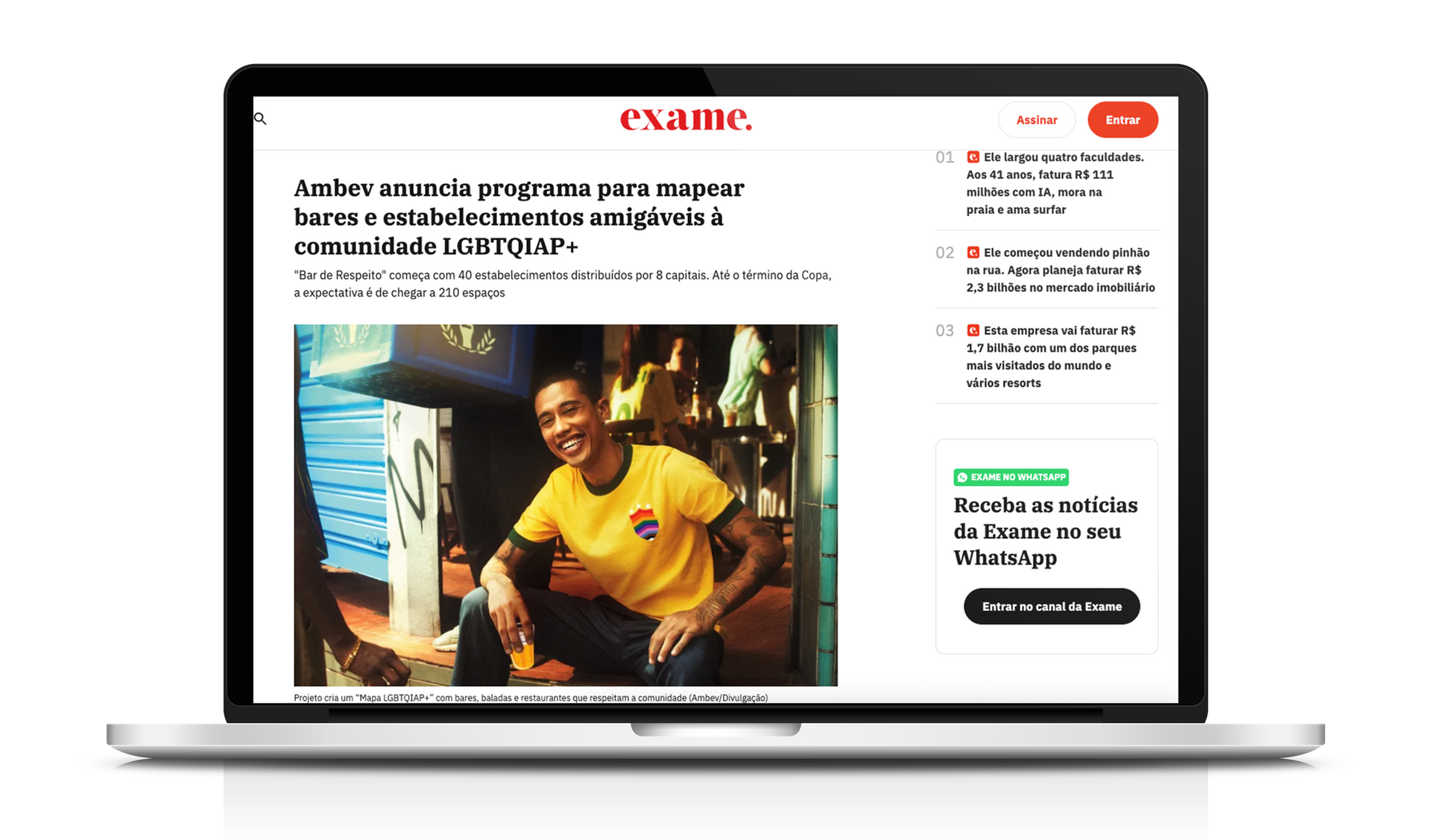 Laptop exibindo um artigo sobre representação LGBTQIA+, com um homem sorridente vestindo uma camisa amarela.