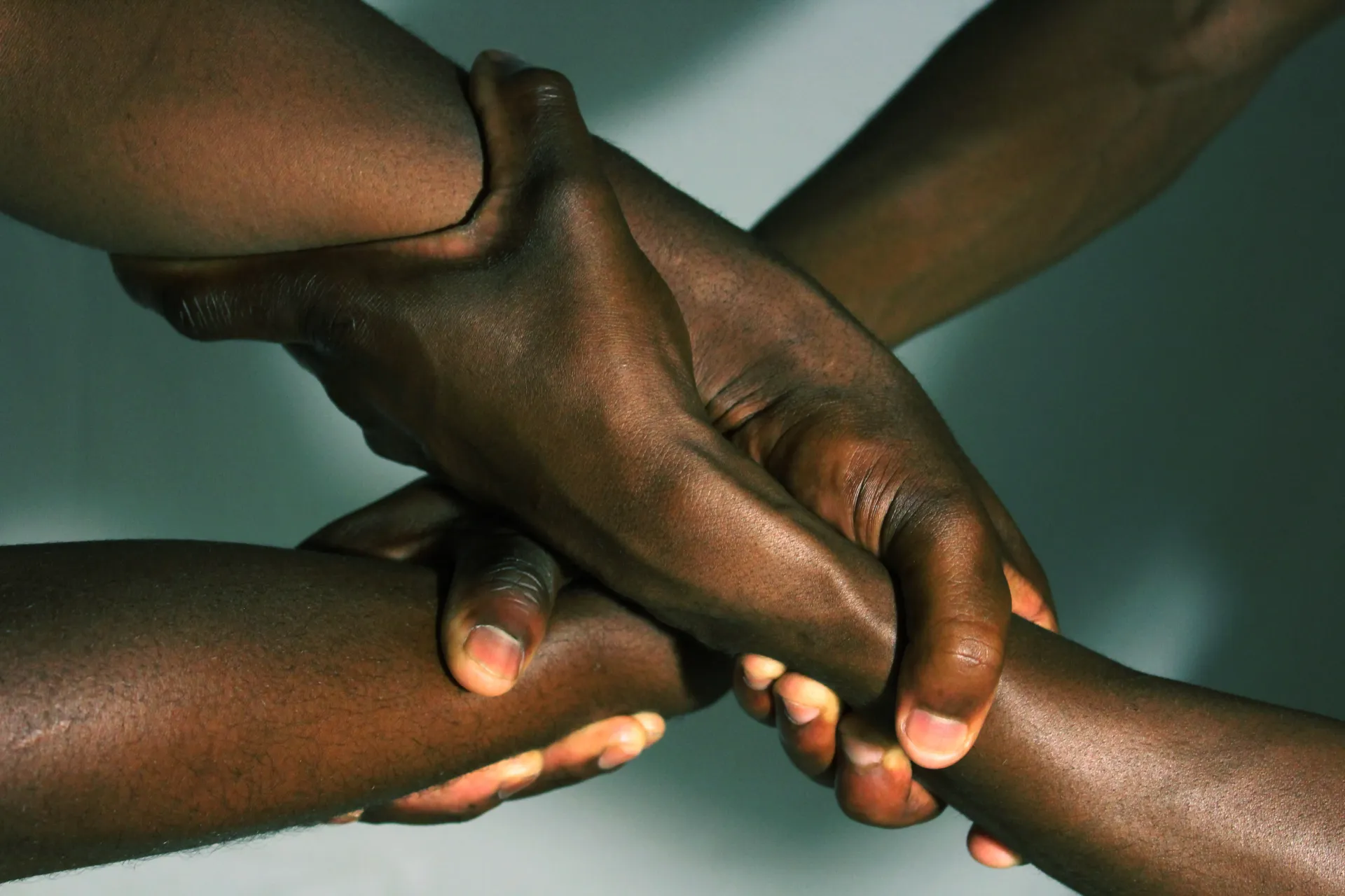 Quatro mãos de pele escura unidas em círculo, simbolizando união e apoio.