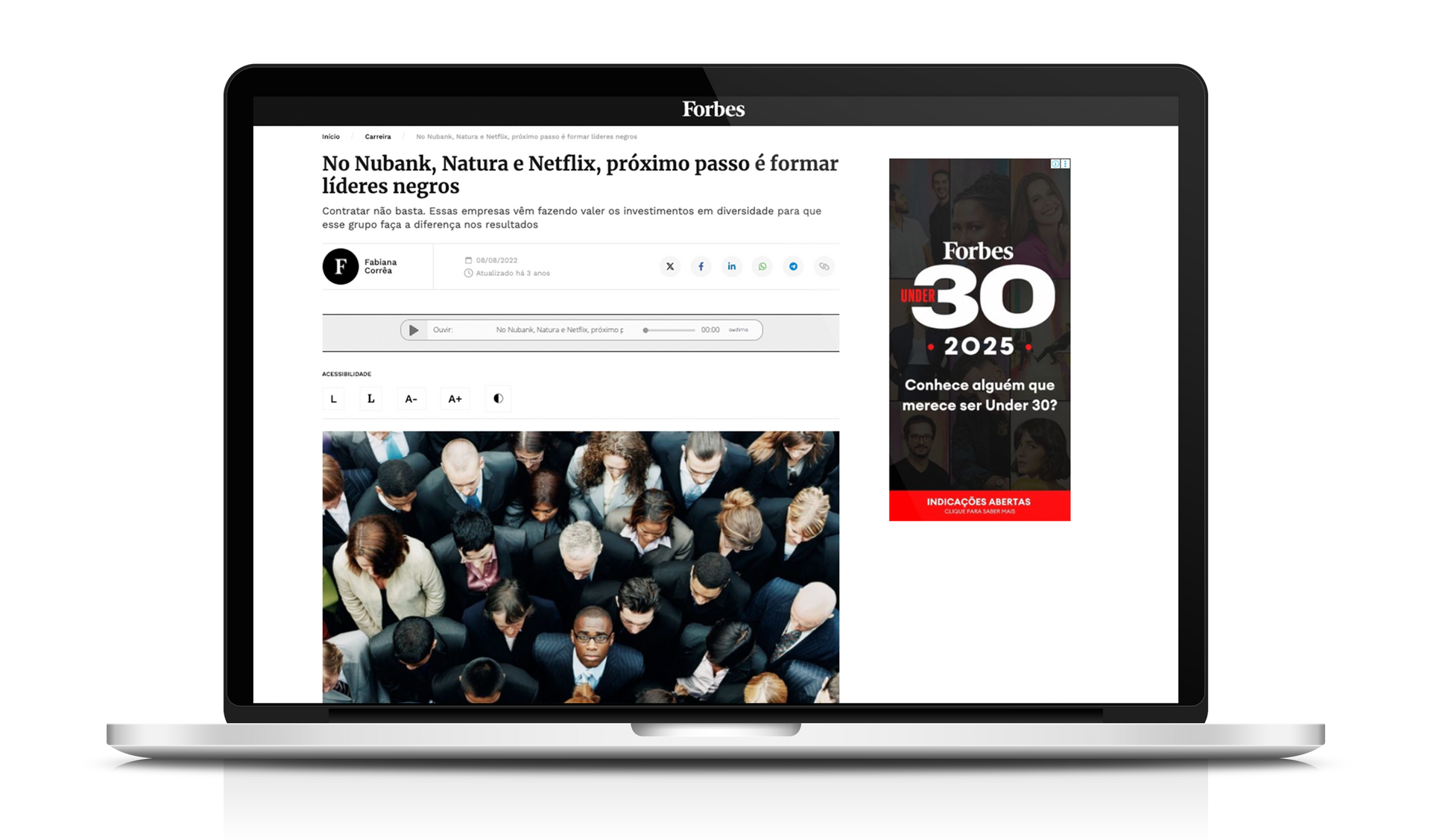 A tela do laptop exibe um artigo da Forbes sobre uma multidão, com um banner de anúncio da Forbes 30 under 30.