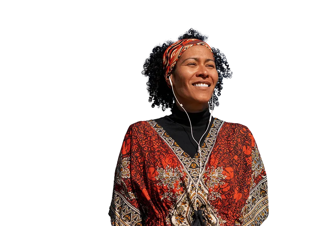 Mulher com cabelos cacheados, blusa laranja estampada e cachecol, ouvindo música com fones de ouvido, sorrindo.