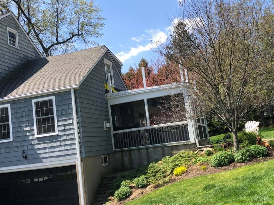 Gray house with a screened-in porch on a hillside, sunny day.