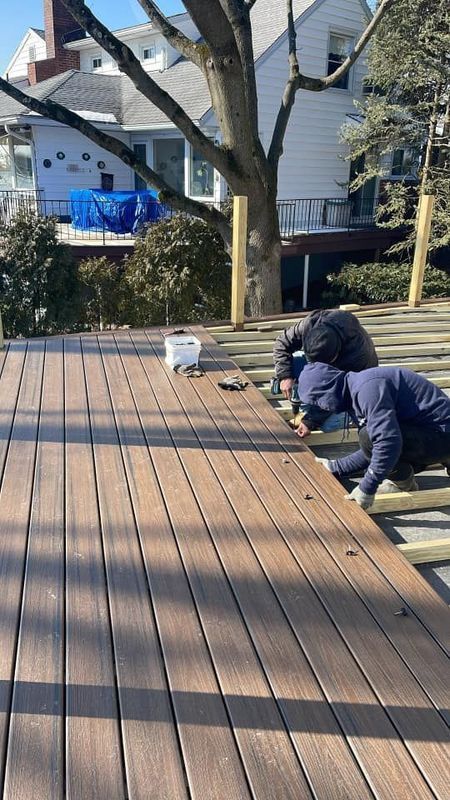 Two people building a deck; laying brown composite boards. Outside, sunny.